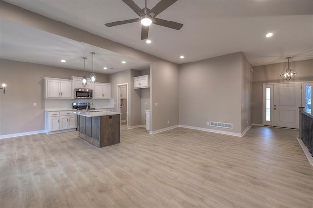 kitchen with an island with sink, white cabinets, hanging light fixtures, stainless steel appliances, and light wood-type flooring