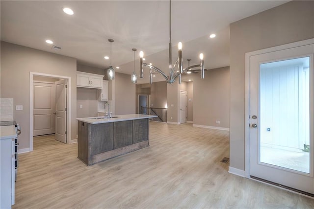 kitchen featuring sink, light hardwood / wood-style flooring, pendant lighting, a kitchen island with sink, and white cabinets