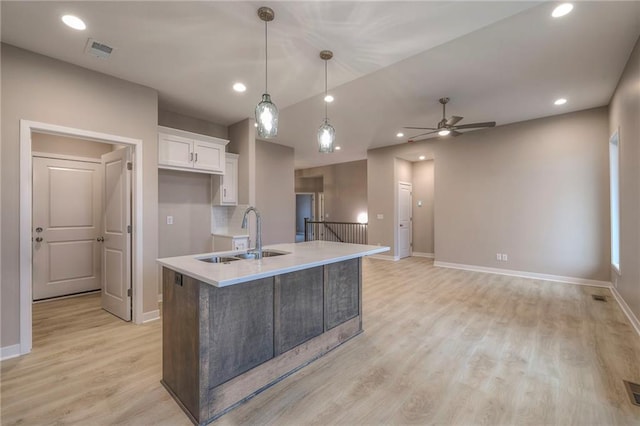 kitchen featuring sink, light hardwood / wood-style flooring, a kitchen island with sink, white cabinets, and decorative light fixtures