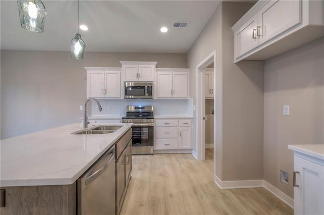 kitchen with sink, light stone counters, pendant lighting, stainless steel appliances, and white cabinets