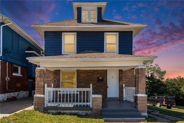 traditional style home featuring stone siding, covered porch, and roof with shingles