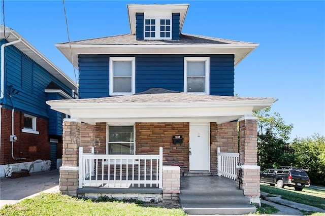 american foursquare style home featuring a porch, stone siding, and a shingled roof