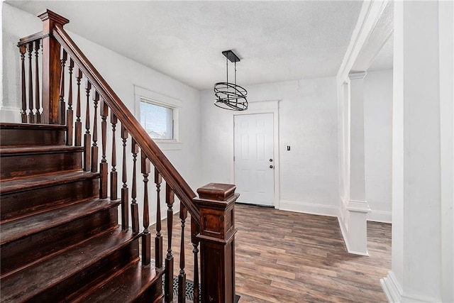 foyer entrance featuring baseboards, an inviting chandelier, dark wood-style flooring, a textured ceiling, and stairs