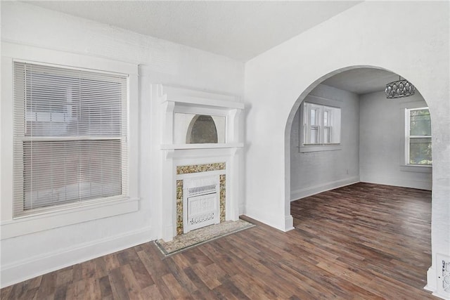 unfurnished living room featuring baseboards, arched walkways, wood finished floors, and a fireplace