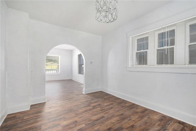 spare room featuring baseboards, arched walkways, an inviting chandelier, and wood finished floors