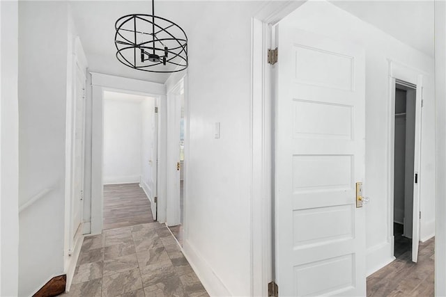 hallway featuring baseboards, a notable chandelier, and stone finish flooring