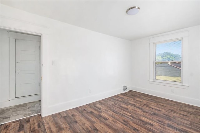 unfurnished room featuring dark wood-type flooring, visible vents, and baseboards
