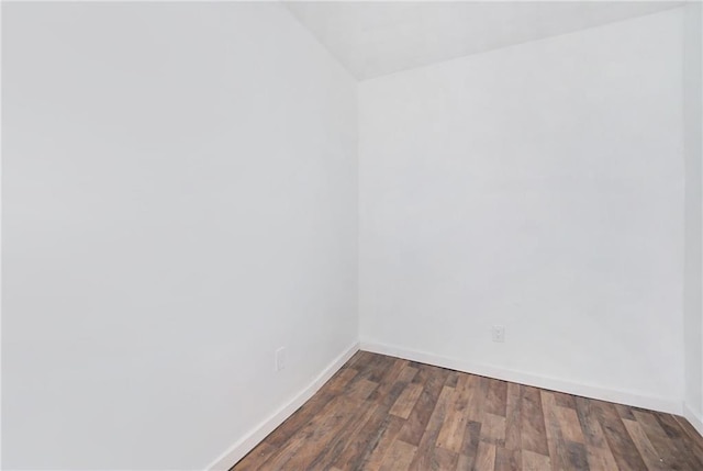 empty room with dark wood-style flooring, baseboards, and vaulted ceiling