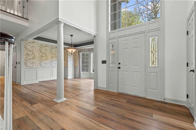 foyer entrance with ornamental molding, a towering ceiling, decorative columns, and hardwood / wood-style floors