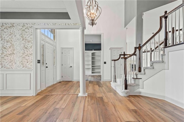 foyer entrance with light wood-type flooring, decorative columns, and a towering ceiling