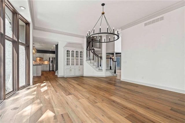 unfurnished dining area with a notable chandelier, hardwood / wood-style flooring, a healthy amount of sunlight, and crown molding