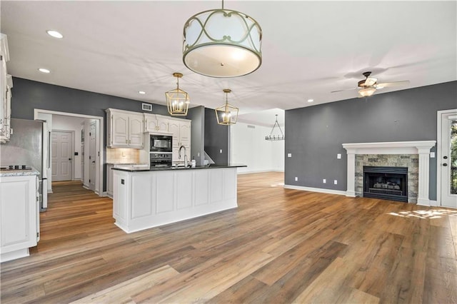 kitchen with ceiling fan, a stone fireplace, light hardwood / wood-style flooring, white cabinetry, and black microwave