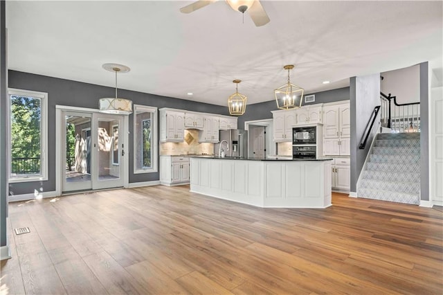 kitchen with hanging light fixtures, white cabinets, backsplash, light wood-type flooring, and black appliances