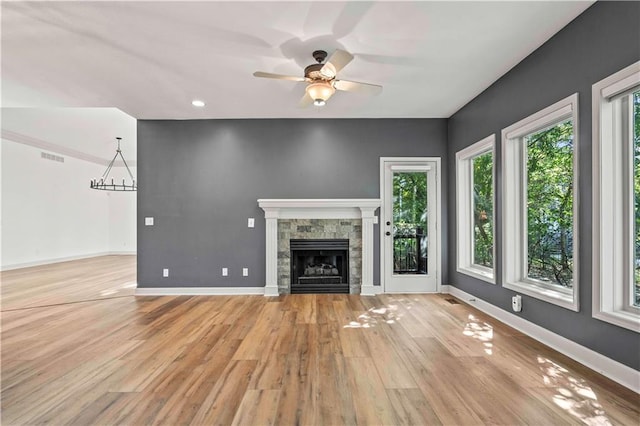 unfurnished living room featuring ceiling fan, a stone fireplace, and light wood-type flooring