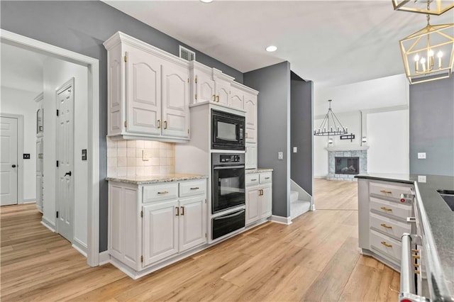 kitchen with light wood-type flooring, white cabinets, black appliances, backsplash, and decorative light fixtures