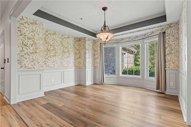 unfurnished dining area featuring a raised ceiling, light wood-type flooring, and ornamental molding