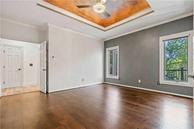 empty room with a tray ceiling, crown molding, dark hardwood / wood-style flooring, and a healthy amount of sunlight