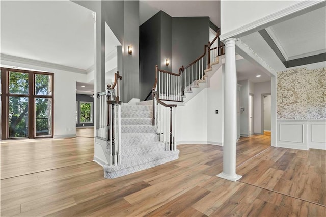 staircase featuring wood-type flooring, decorative columns, and crown molding