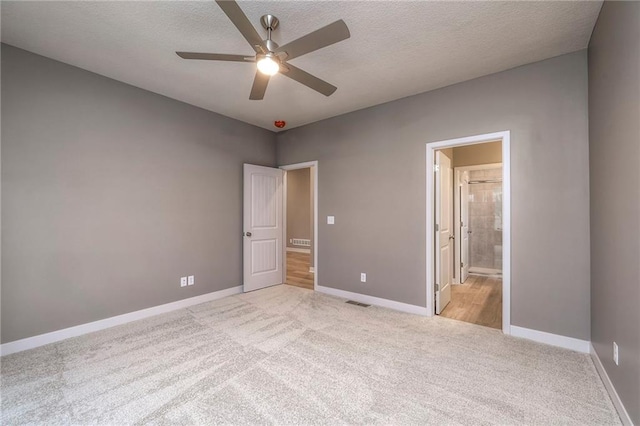 unfurnished bedroom with ceiling fan, light colored carpet, ensuite bathroom, and a textured ceiling