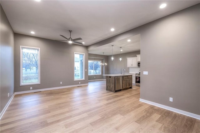 kitchen with pendant lighting, an island with sink, sink, stainless steel appliances, and light wood-type flooring