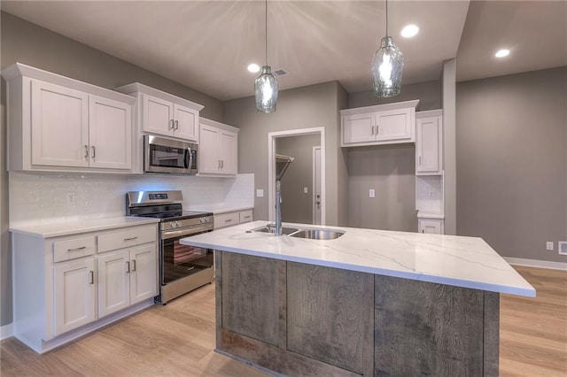 kitchen with stainless steel appliances, an island with sink, hanging light fixtures, and white cabinets