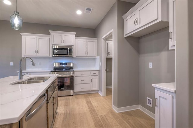 kitchen featuring sink, white cabinetry, light stone counters, hanging light fixtures, and appliances with stainless steel finishes