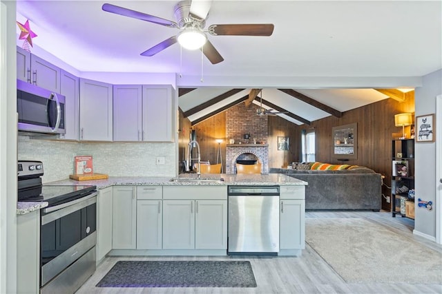 kitchen featuring sink, kitchen peninsula, wooden walls, stainless steel appliances, and light wood-type flooring