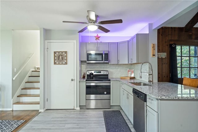 kitchen with light wood-type flooring, sink, decorative backsplash, stainless steel appliances, and light stone countertops