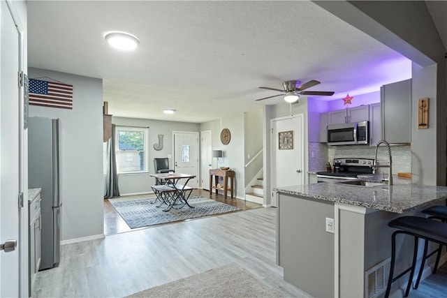 kitchen with light hardwood / wood-style floors, kitchen peninsula, a kitchen bar, stone counters, and appliances with stainless steel finishes