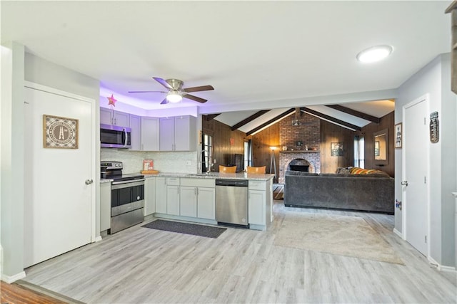 kitchen with kitchen peninsula, wood walls, stainless steel appliances, ceiling fan, and light hardwood / wood-style flooring