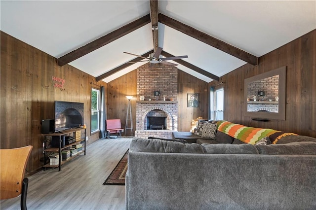 living room with ceiling fan, vaulted ceiling with beams, wood walls, wood-type flooring, and a fireplace