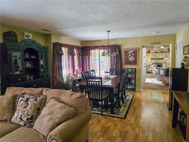 dining area featuring a notable chandelier, a textured ceiling, a fireplace, and hardwood / wood-style floors