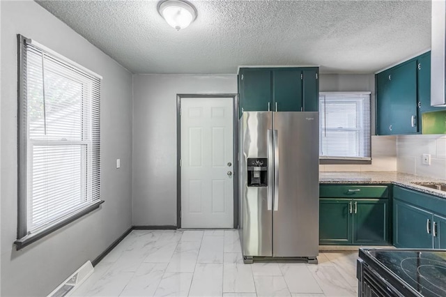 kitchen featuring stainless steel refrigerator with ice dispenser, a textured ceiling, plenty of natural light, and electric range oven