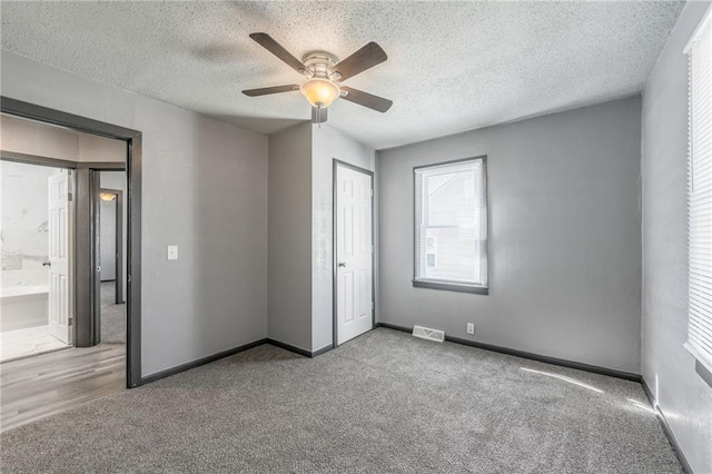 unfurnished bedroom with ceiling fan, a textured ceiling, carpet flooring, ensuite bathroom, and a closet