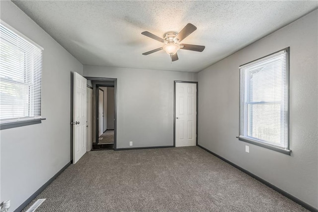 unfurnished bedroom featuring dark carpet, a textured ceiling, and ceiling fan