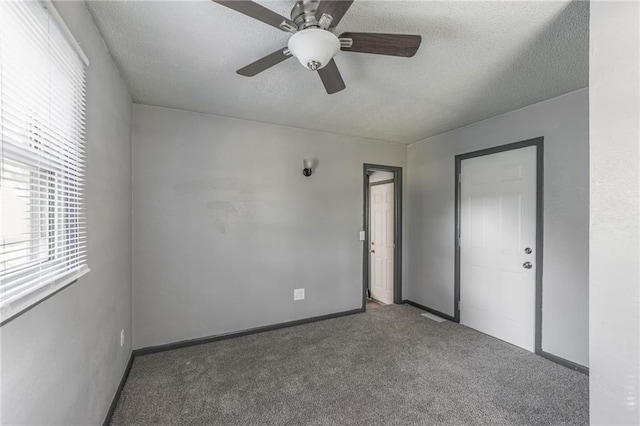 empty room featuring ceiling fan, a textured ceiling, and dark colored carpet