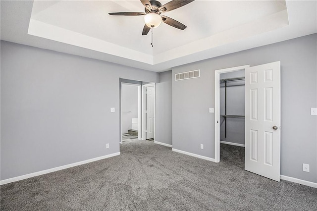 unfurnished bedroom with carpet flooring, ceiling fan, a raised ceiling, and a walk in closet