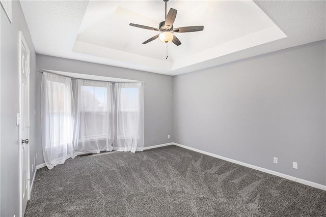 carpeted spare room with a raised ceiling and ceiling fan