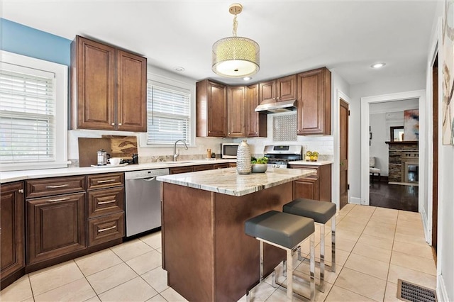 507 E 75th St, Kansas City, MO 64131 - kitchen featuring under cabinet range hood, light tile patterned floors, appliances with stainless steel finishes, and a kitchen bar