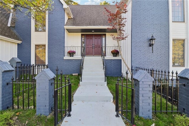 view of exterior entry with a gate, brick siding, fence, and roof with shingles