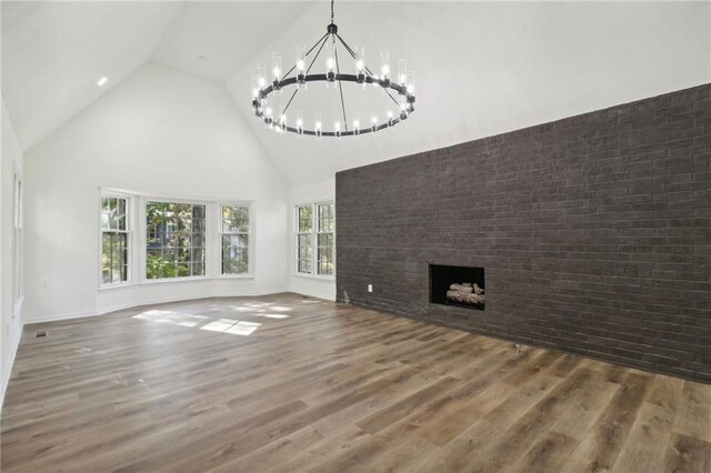 unfurnished living room with a notable chandelier, high vaulted ceiling, brick wall, and hardwood / wood-style floors