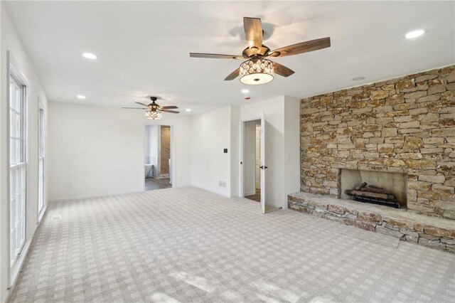 unfurnished living room with a stone fireplace, light carpet, and ceiling fan