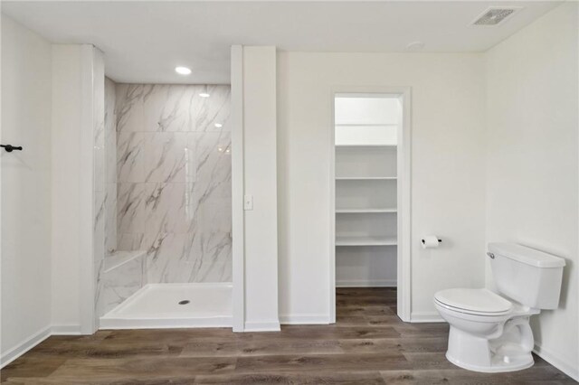 bathroom featuring a tile shower, toilet, and hardwood / wood-style flooring