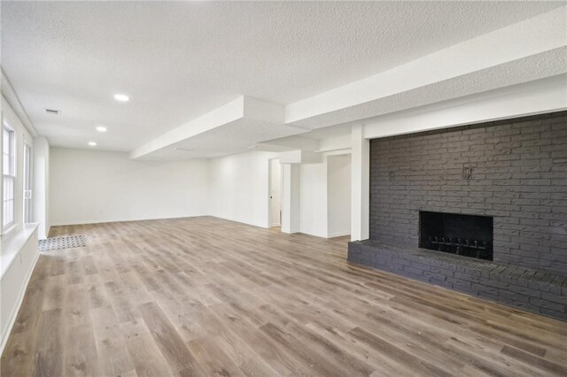 unfurnished living room with a textured ceiling, wood finished floors, recessed lighting, and a brick fireplace