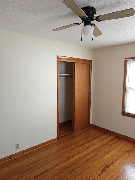 unfurnished bedroom with a textured ceiling, wood-type flooring, ceiling fan, and a closet