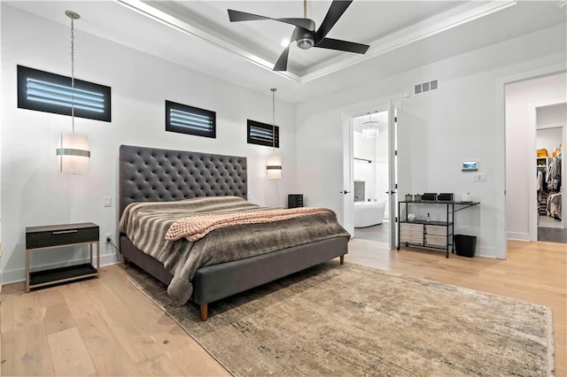 bedroom featuring ceiling fan, connected bathroom, hardwood / wood-style flooring, a tray ceiling, and a spacious closet