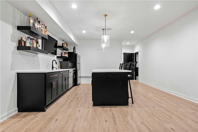 kitchen with hanging light fixtures, sink, a center island, a breakfast bar area, and light wood-type flooring