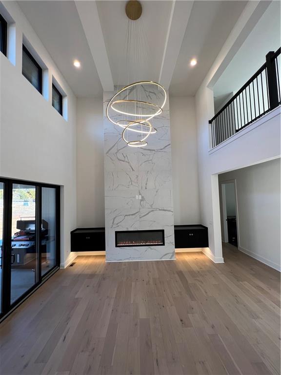 unfurnished living room featuring a high ceiling, a fireplace, hardwood / wood-style floors, and an inviting chandelier