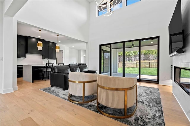 living room with a high ceiling, a fireplace, an inviting chandelier, and light hardwood / wood-style flooring