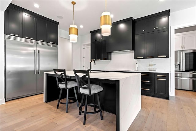 kitchen with stainless steel fridge, stainless steel built in fridge, pendant lighting, and an island with sink